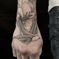 Alan Lott hand tattoo of a swallow with flowers. Tattoo done in black and grey.